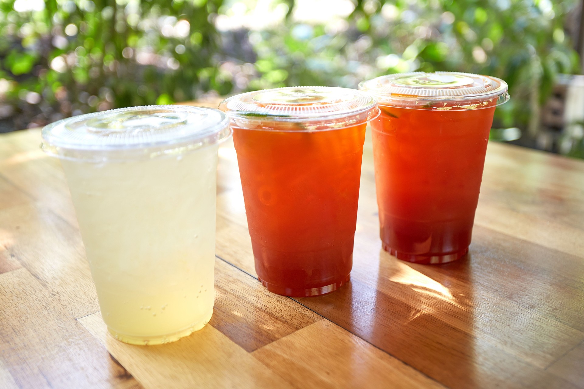 Iced lemon tea and honey lemon soda in plastic cups with lids placed on wooden tables.