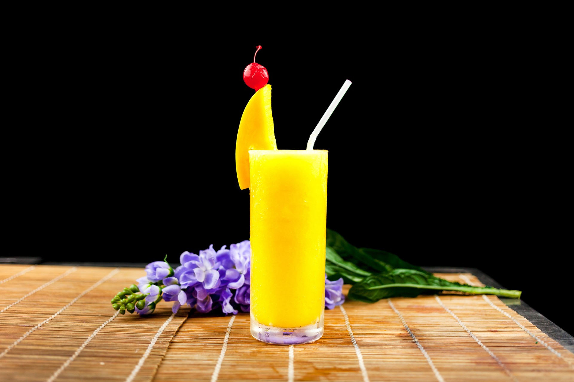 Mango juice and fruit on glass near flower